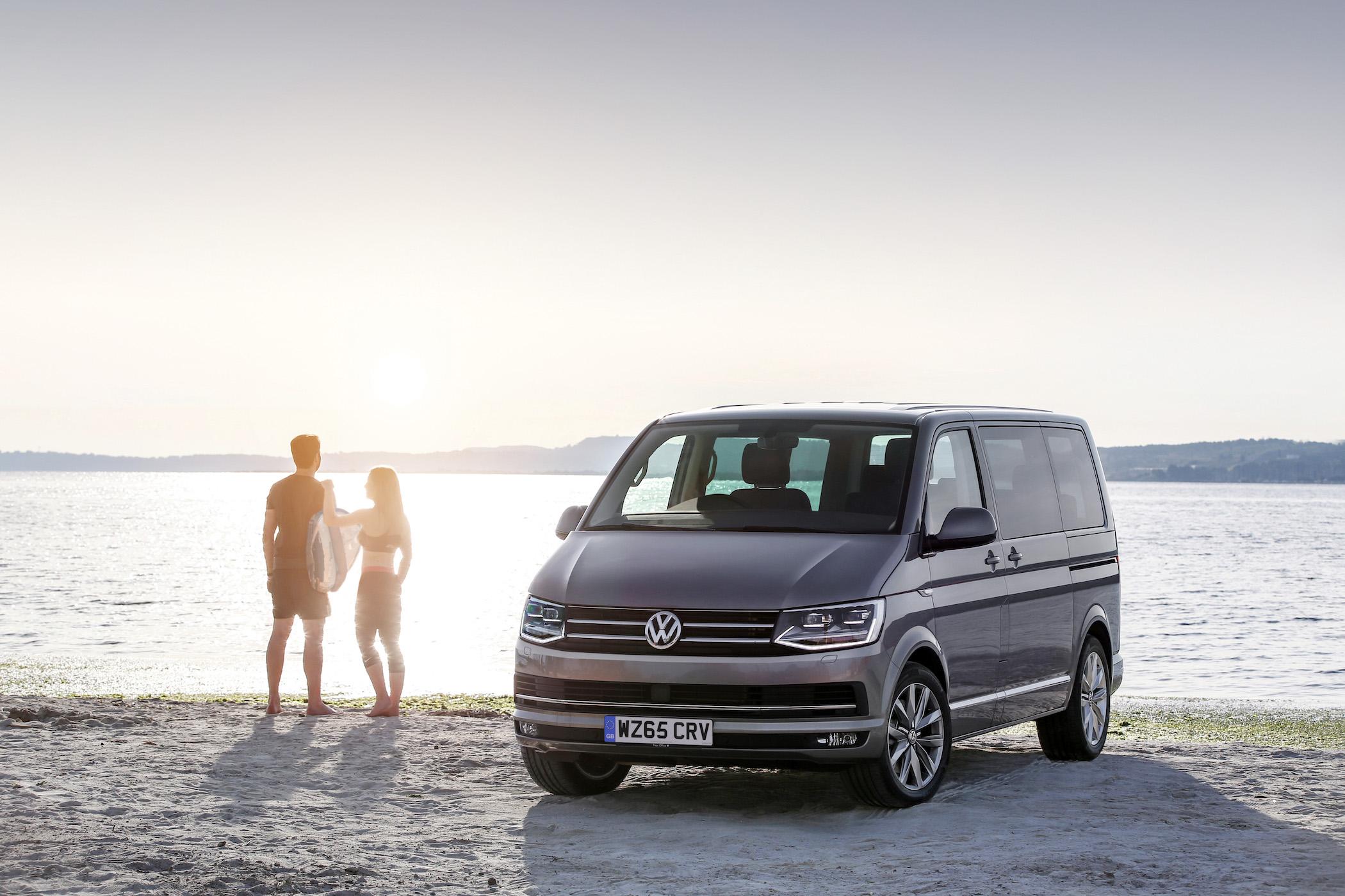 volkswagen caravelle on the beach next to two people