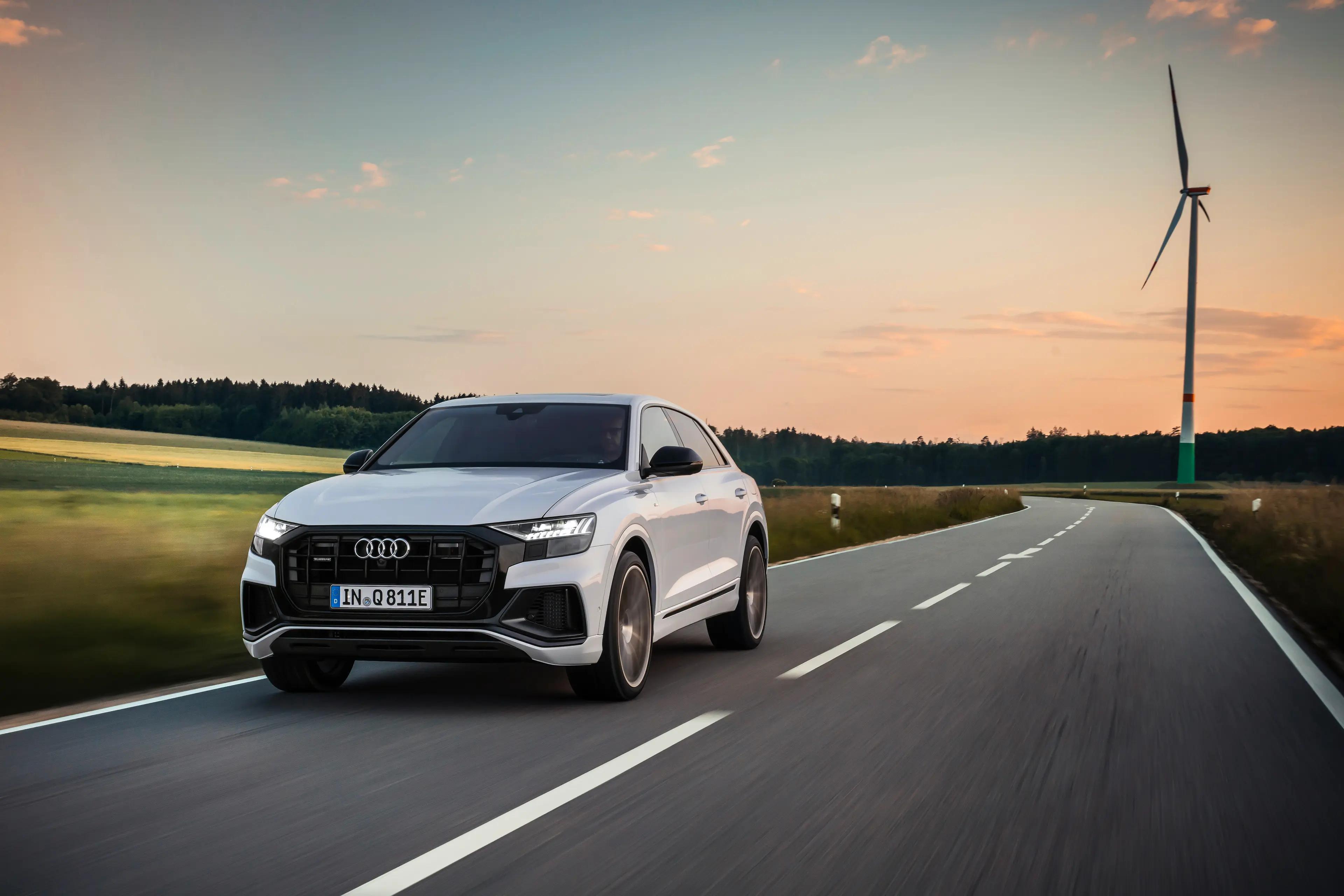 A white Audi Q8 driving down a countryside road at sunset 